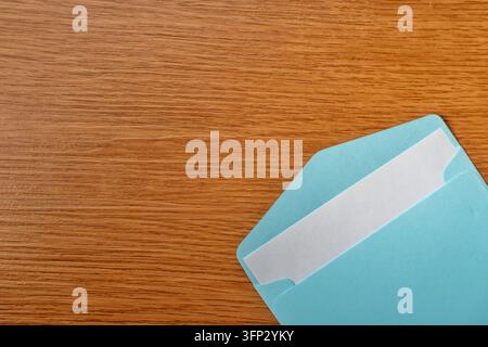 Open blue envelope with a blank white paper card inside on a wooden table. Mail, invitation, letter, newsletter, or business contact concept. Stock Photo