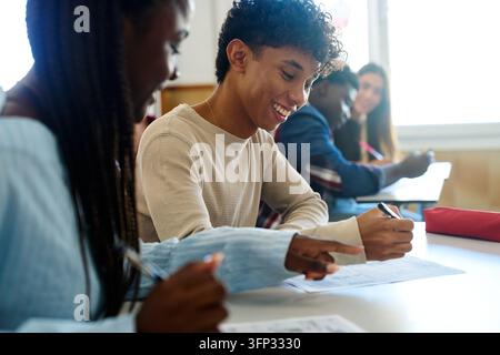 Young students working together at a desk, learning and studying with a teacher in a modern school classroom environment Stock Photo