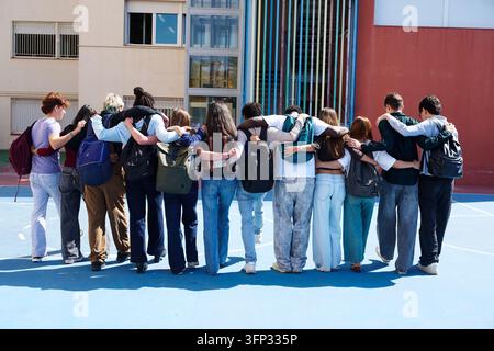 Group of diverse students standing together on a schoolyard with arms around each other, showing unity and friendship Stock Photo