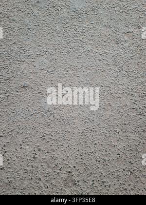 A close up view of a coarse grey asphalt road surface. The texture shows gritty details of stone aggregate and bitumen. Stock Photo