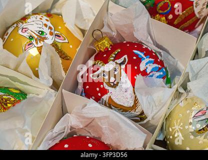Closeup of colorful hand painted Christmas baubles decorated with sheep and goat illustrations, nestled in tissue paper inside open storage boxes Stock Photo