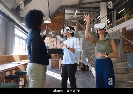 Diverse coworkers demonstrating VR training in open-plan loft with tablet and white headsets Stock Photo