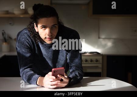 African American man leaning on kitchen island, holding pink smartphone, looking up Stock Photo