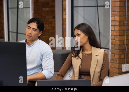 Diverse coworkers wearing business attire working at shared modern workspace with large monitor Stock Photo