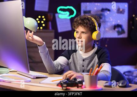 Online learning and digital education, boy with headphones using computer for remote school and gaming in bedroom with neon lights at night Stock Photo