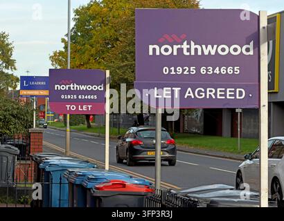 Several purple Northwood boards beside a road advertise LET AGREED, with vehicles, trees and business premises in the background. Stock Photo