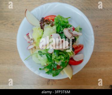 A fresh salad beautifully presented on a ceramic plate, set atop a wooden table, offering a top-down view of the vibrant green and red ingredients Stock Photo