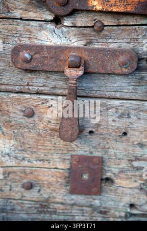 Rusty iron latch on weathered wooden door with peeling grain, old fasteners, and aged patina showing texture and decay Stock Photo