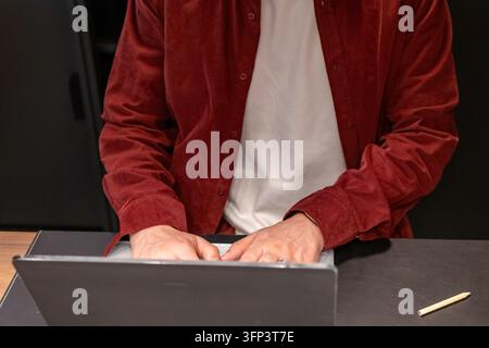 Cropped view of male hands typing on a laptop keyboard at a dark leather desk pad with a wooden pencil lying nearby. Concept of office work, productiv Stock Photo