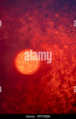 Condensation water drops on a wet window with blurry sun disk, orange light shining through small water drops on transparent glass surface Stock Photo