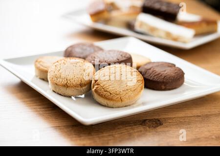 Close-up of assorted Spanish shortbread cookies, including vanilla and chocolate varieties, arranged on a white plate on a wooden table. Traditional s Stock Photo