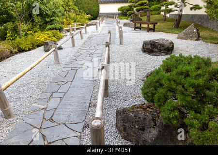 A landscaped garden scene with sculpted evergreen trees, gravel, rocks, stone paving, shrubs, and a rustic wooden rail at Blühendes Barock in Ludwigsb Stock Photo