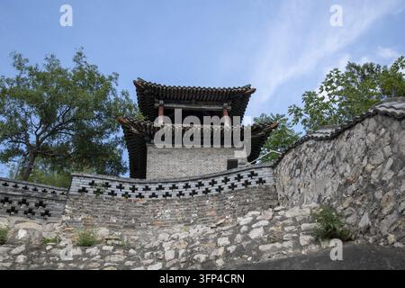 A traditional brick tower with tiered tiled roofs rising behind a curved decorative wall and stone retaining walls in Handan, Hebei, China. Stock Photo