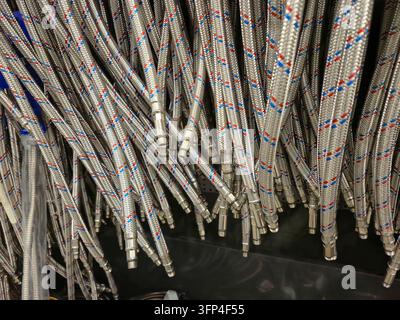A large amount of flexible woven stainless steel hoses with colored threads are neatly arranged on storage shelves, ready for sale Stock Photo