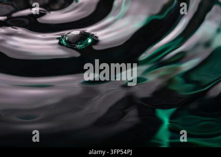 285.A detailed, macro close-up of a perfectly formed air bubble floating on a dark, reflective water surface with abstract ripples. The soft lighting Stock Photo
