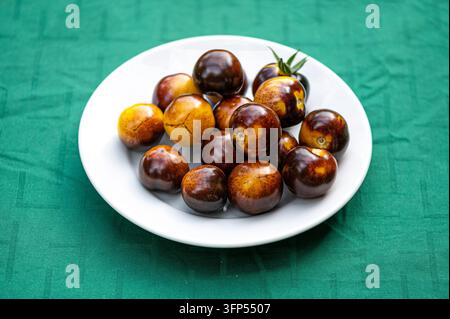 Fresh cherry tomatoes of different varieties on a plate on the blurred background, close-up Stock Photo