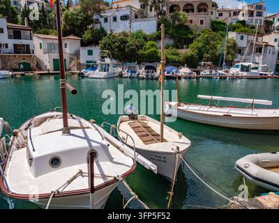 Traditional white fishing boats moored in the turquoise waters of Cala Figuera's protected harbor, surrounded by Mediterranean stone architecture and Stock Photo