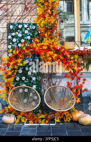 Cozy autumn seating area decorated with colorful maple leaves and pumpkins, charming seasonal outdoor display with wicker chairs and warm lights. Stock Photo