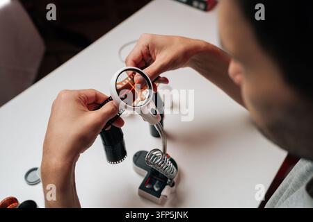 Over shoulder view of person examining 35mm film negative with magnifying lens. Clean white workspace. Focus on hands and detailed inspection. Concept Stock Photo