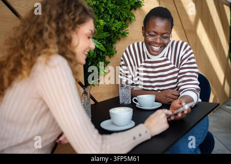 Diverse friends enjoying coffee sharing content on smartphone Stock Photo