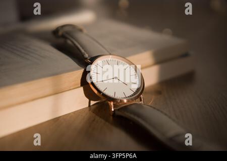 Elegant minimalist wristwatch resting on stack of vintage books in warm sunlight – ideal mockup for timepiece advertising, time management articles Stock Photo