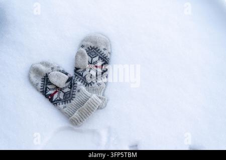 Knitted Winter Mittens with Ornament Pattern Lying on White Snow Top View background. Lost Gloves Stock Photo