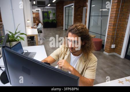 Diverse coworkers working in open-plan office, male using large monitor and laptop Stock Photo