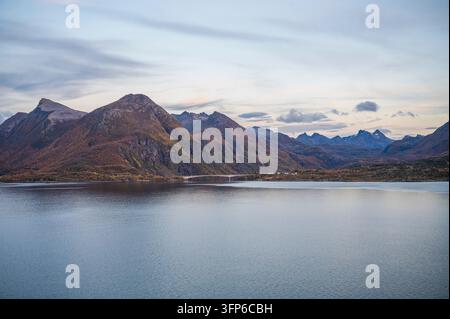 A serene landscape featuring a calm lake with majestic mountains in the background, under a soft, pastel sky, Sortland, Norway Stock Photo