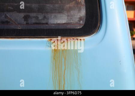 Rusting body in an old blue car. Weather damage below window in vehicle. Stock Photo