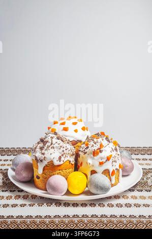 A collection of beautifully decorated Easter cakes and colorful eggs are presented on a white plate, set against a background of a traditional embroid Stock Photo