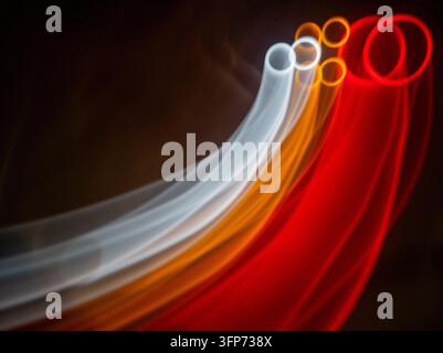 An abstract light painting featuring smooth, flowing lines of white, orange, and red light streaking across a dark background, creating a dynamic visu Stock Photo