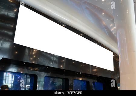 Large blank digital screen hangs in modern lobby. Sleek metallic walls and ceiling lights reflect off glossy surfaces. Empty space suggests advertisin Stock Photo