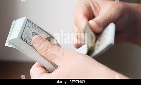 A person holding several hundred dollar banknotes. Male hands counting a stack of hundred dollar bills Stock Photo