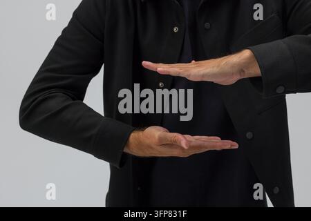 Man in black shirt holding two open hands parallel to each other. Concept for holding an invisible object, framing virtual holograms, size measurement Stock Photo