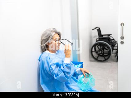 Medical worker feeling burnout and fatigue, sitting on floor in surgery waiting area Stock Photo