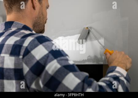 Handyman painting plaster patch with paint roller after wall repair Stock Photo
