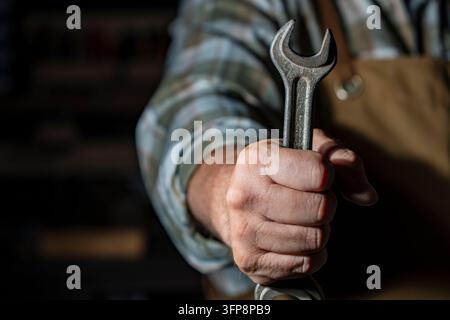 Mechanic hand holding metal wrench tool in workshop. Close up of worker hand holding spanner tool. Plumber, repairman or mechanic expert in uniform re Stock Photo