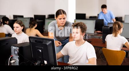 Schoolboy using computer and teacher helping to him in classroom Stock Photo