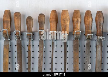 Old vintage rasps with wooden handles hanging on steel wall as background. A set of files and rasps for hand sanding, close up. Hand work tool in work Stock Photo