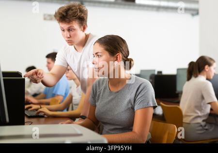 Schoolboy using computer and teacher helping to him in classroom Stock Photo