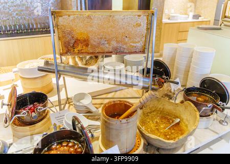 Horizontal shot of pure golden honey flowing down a steel rack from a large honeycomb frame at a premium resort breakfast buffet. Stock Photo
