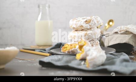 A stack of homemade sweet Portuguese donuts coated in white sugar glaze is artfully arranged on a dark plate, complemented by a milk bottle in the sof Stock Photo