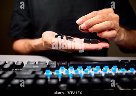 Hand holding removed black computer keycaps over keyboard Stock Photo