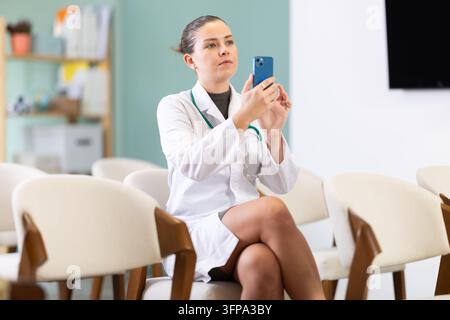 Young woman, a medical university student, at a lecture takes a photo of the lecture on her mobile phone. Young doctor scans the qr code of the presen Stock Photo