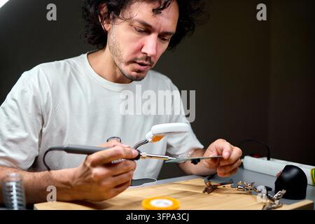 Man soldering electronic circuit on workbench under focused light Stock Photo