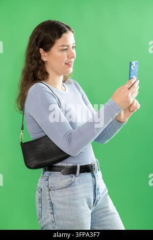 Female model uses mobile device to photograph or scan code on green backdrop during video recording Stock Photo