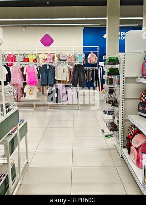 Kirov, Russia - August 19, 2026: Retail interior shows childrens dresses, shirts, jeans and accessories on racks with backpacks and stationery nearby Stock Photo