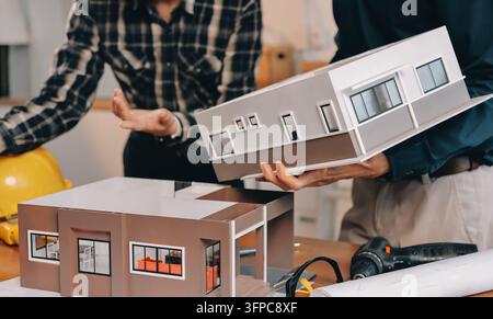 Asian architect and engineer team checking architectural house model using measuring tape on the table at office studio. Stock Photo