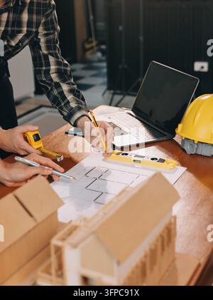 Asian architect and engineer team checking architectural house model using measuring tape on the table at office studio. Stock Photo