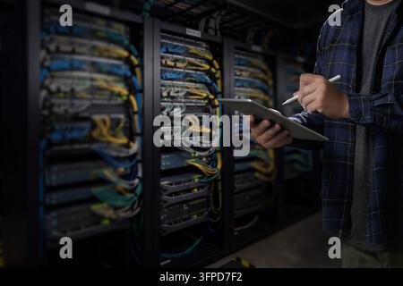 man engineer it support using tablet and stylus beside server racks in a data center, supporting network monitoring, IT infrastructure review and tech Stock Photo
